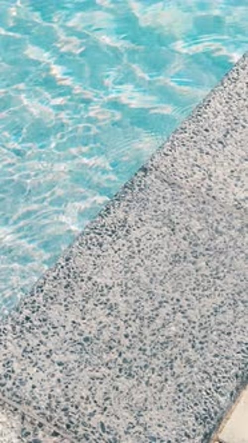 Klares blaues Wasser im Pool. Stufen in den Pool. Der Rand des Pools ist mit einem grauen Bordstein versehen