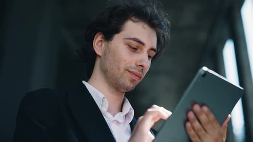 Hübscher kaukasischer männlicher Manager nutzt digitales Tablet in der Nähe des Business Centers, um Apps zum Scrollen von SMS zu senden