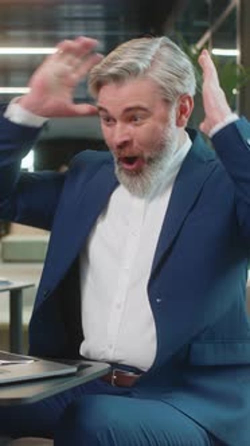 Caucasian Bearded Businessman Working on Laptop Surprised By Sudden Victory in Modern Hotel Lobby