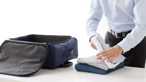 Man packing a blue suitcase with folded shirts