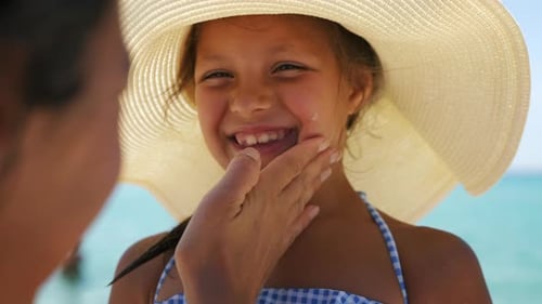 Nahaufnahme einer jungen Mutter, die schützende Sonnencreme oder Sonnencreme auf ihr kleines Happy S aufträgt