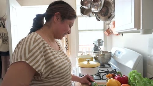Woman chopping cucumber in a brightly lit kitchen