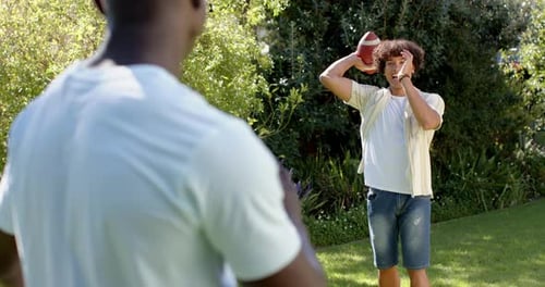 Playing catch with football, two multiracial male friends enjoying outdoor hangout in park