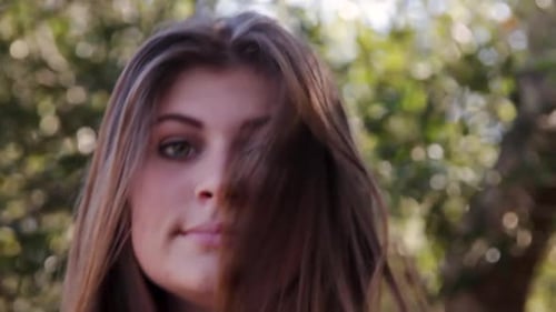 Mujer morena levanta la cabeza en el marco y sonríe y se mueve el pelo en un día ventoso