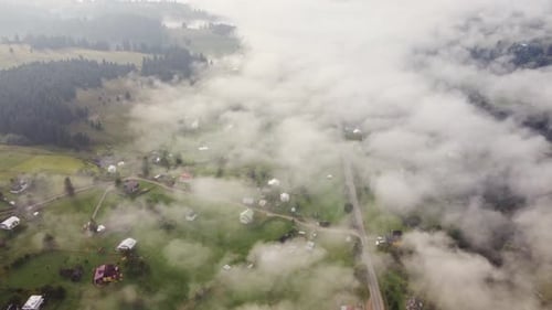 Flug über ein kleines Dorf inmitten der grünen Berge im Nebel