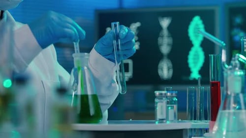 A Female Scientist Pipettes a Green Liquid Into a Glass Test Tube and Examines the Sample