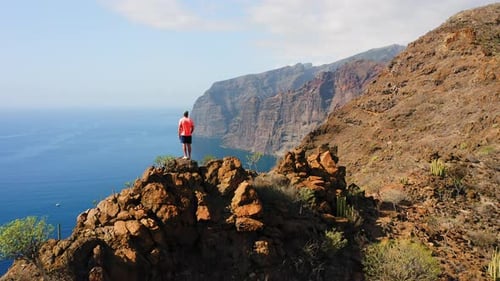 Man Stands Atop Rocky Mountain Overlooking Ocean