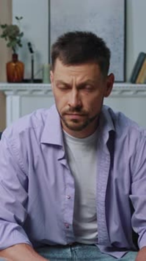 A Casually Dressed Man Sits in a Cozy Indoor Setting Reflecting Deeply with Concentration