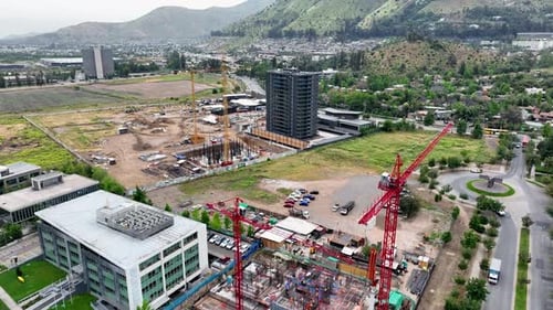 Forward drone aerial of construction site with red cranes, foundation work, high-rise tower,