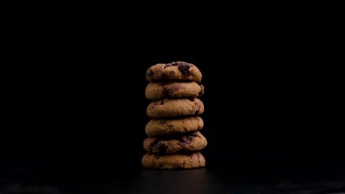 Stapel wunderschöner vegetarischer, goldbrauner Kekse mit Schokolade, die sich gegen einen schwarzen Hintergrund dreht