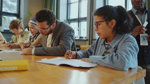 Élèves immigrants écrivant dans des cahiers pendant un cours dans une école de langues