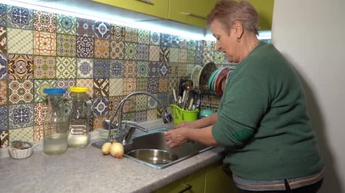 An Elderly Woman Peels Potatoes Mash Potatoes in the Kitchen Sink Cook Vegetables at Home