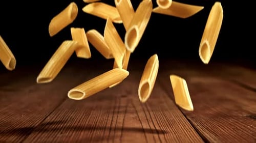 Penne Pasta Falling on Wooden Table in Slow Motion