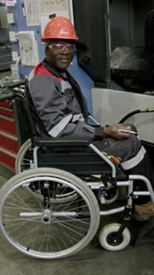 Vertical Portrait of Positive Workman Posing in Wheelchair at Factory