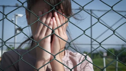 Child Covering Face near Chain-Link Fence