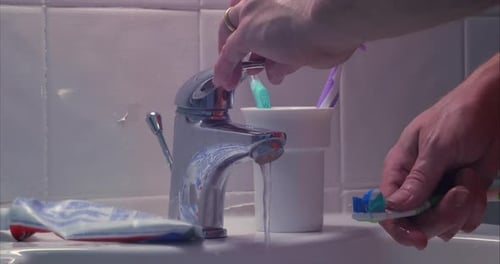 Man soaks toothbrush under tap before brushing teeth over sink, close up shot