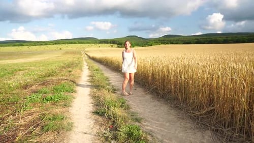 Happy Free Young Woman Running Dancing and Spinning Around Amid Wheat Field Touching Ears Against a