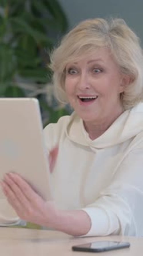 Excited Senior Woman Celebrating Success Using Tablet Device