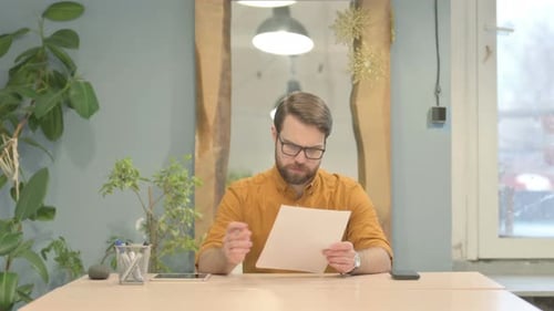 Man Reads Document at Desk Indoors