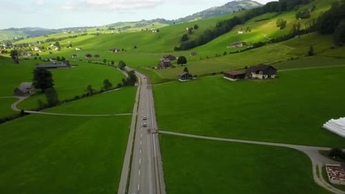 flyover a road surrounded by green fields. following a car