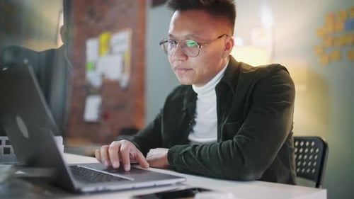 Young Man Works on Laptop at Desk