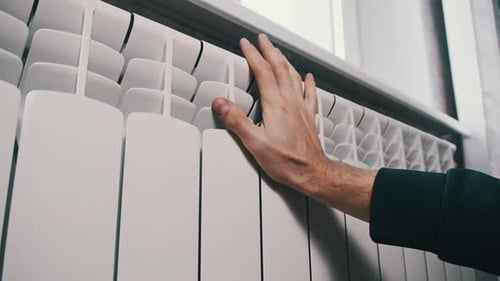 Hand Touches a White Radiator by Window