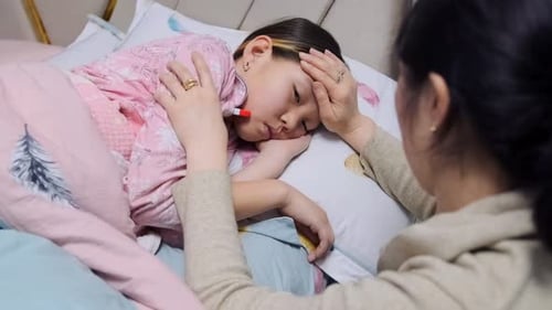 Mother Checking Temperature of Sick Child in Bed