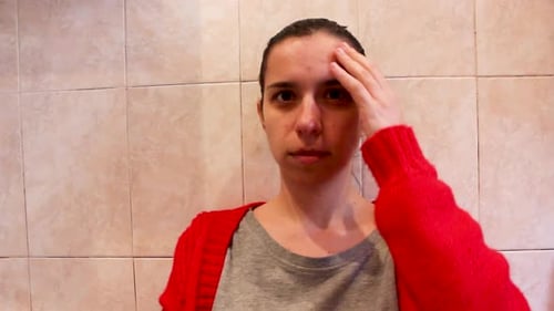 Jeune femme acnéique touchant la peau de son visage dans la salle de bain, gros plan à mi-distance