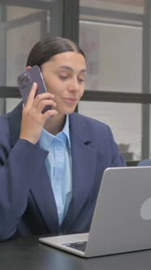 Woman in Blazer Talks on Phone at Desk