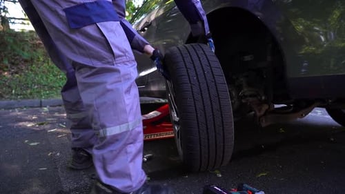 Roadside assistance. Mechanic changes flat tire. Man wearing overall. Broken car.