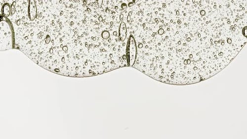 Gel fluide cosmétique transparent avec des bulles de molécules s'écoulant sur la surface blanche lisse