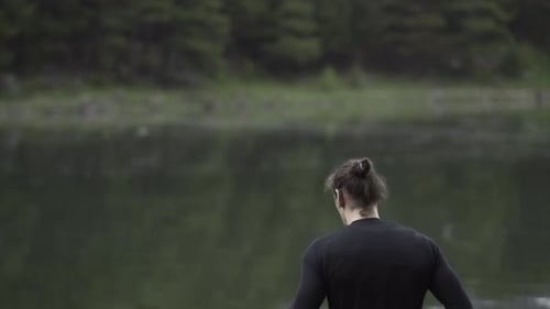 Spanish Man with Ponytail Climbs on a Rock and Opens His Arms in a Lake