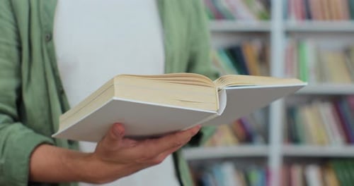 Nahaufnahme eines unkenntlichen Mannes, der in einer öffentlichen Bibliothek ein Buch liest, Seiten umblättert und recherchiert