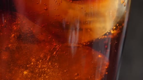 Macro close-up of a cold drink as the fizzy bubbles rise around the ice cubes.
