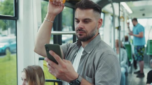 A Man with Facial Hair is Using a Cell Phone While Riding a Bus