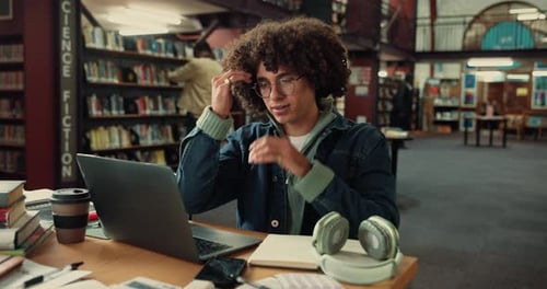 Tired man, student and headache with laptop at library for burnout, fatigue or overworked
