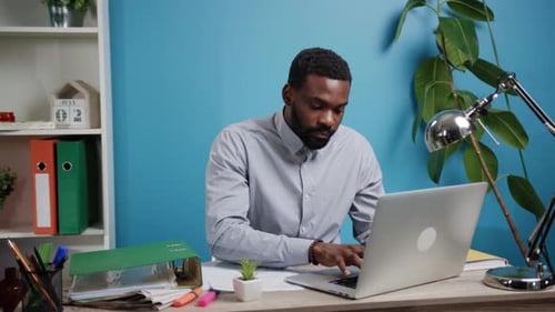 A Professional Man is Effectively Working in His Home Office Utilizing a Laptop for Tasks