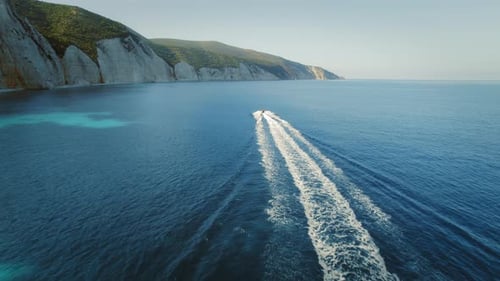 Speedboat cruising away leaving a trail on the calm blue sea by cliffs in Grecce