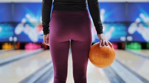 Woman in Sport Leggings Holding Orange Bowling Ball at Alley, Leisure Game