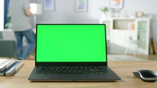 Modern Laptop with Green Mock-up Screen Display Standing on the Desk in the Cozy Living Room. Man w