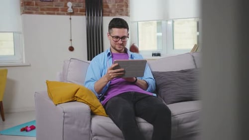Happy Young Man Use Tablet Computer at Home Sitting on Sofa Smiling Modern Day Close Up Hobby