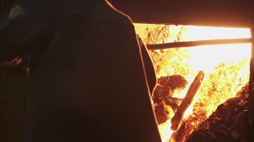 Industrial Worker Tending to Furnace Flames with Shovel