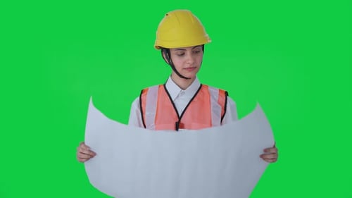 Happy Indian female architect looking through the blueprint Green screen