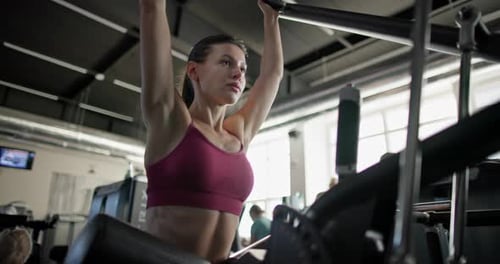 Young Beautiful Woman in Sportswear Exercising and Doing Arm Pullups on a Machine in a Gym