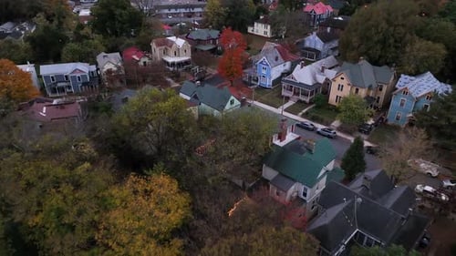 Red colored tree in american neighborhood with colorful houses at dusk. Cloudy autumn day in USA. Fa
