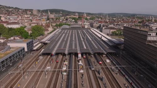 Vorwärts fliegen über dem überdachten Bahnsteig des Hauptbahnhofs und Personenzügen auf den Gleisen Luftbild von