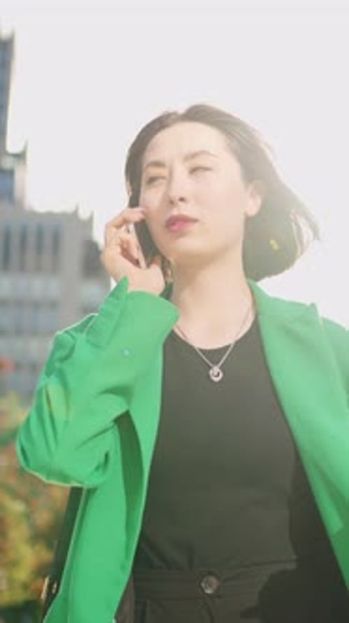 Femme souriante en blazer vert parlant sur un smartphone à l'extérieur en gros plan dans une ville lumineuse