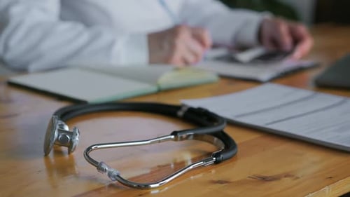 Stethoscope and Doctor Writing Notes on Desk