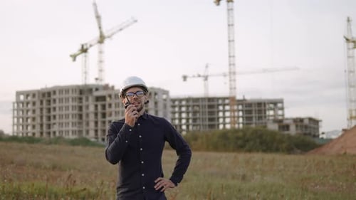 Serious Man Engineer geht und spricht auf einem Walkietalkie in der Nähe der Baustelle