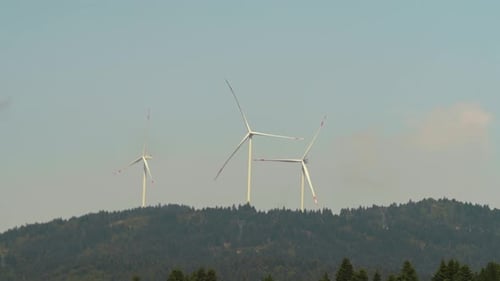 Wind Turbines Spinning on Forested Hill, Daytime
